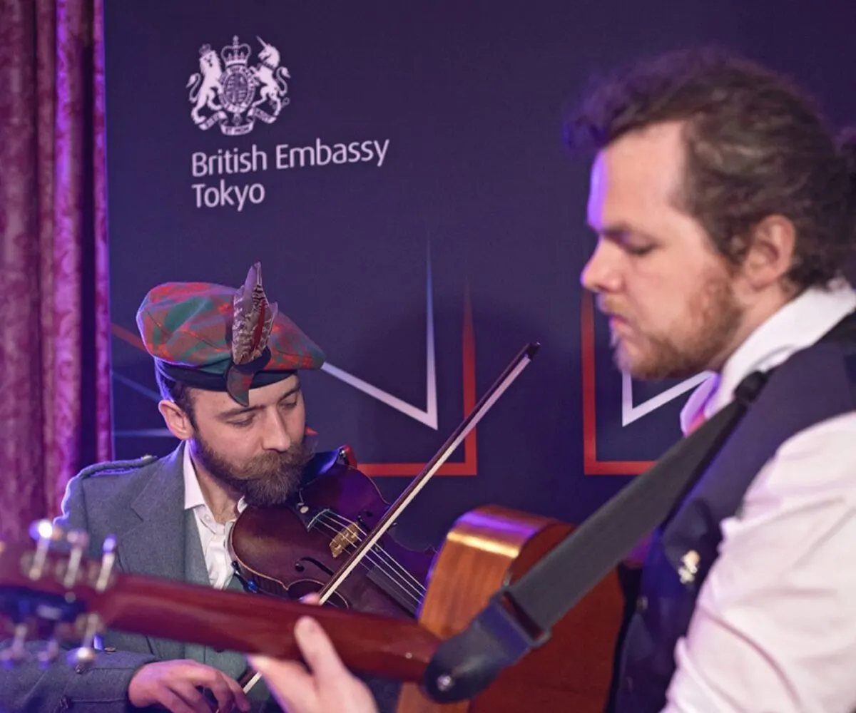 Scottish fiddler and guitarists in full Scottish highland dress playing Scottish trad music at British embassy Tokyo, curated by The Curators of Exiled Scots
